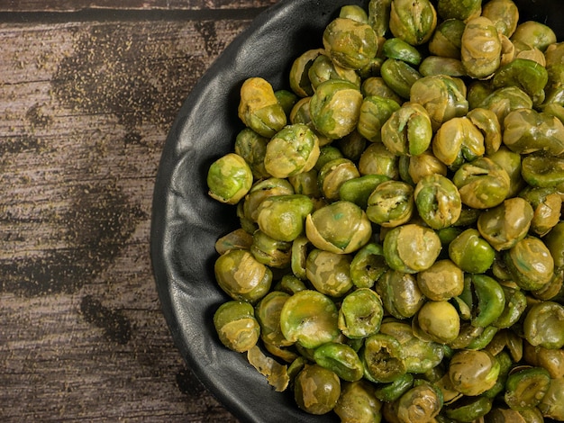 Salted green peas in black bowl on wood table