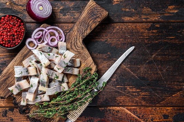 Salted herring fish sliced fillet on a wooden board with thyme. Dark wooden background. Top view. Copy space.