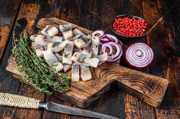 Salted herring fish sliced fillet on a wooden board with thyme on wooden table. Top view.