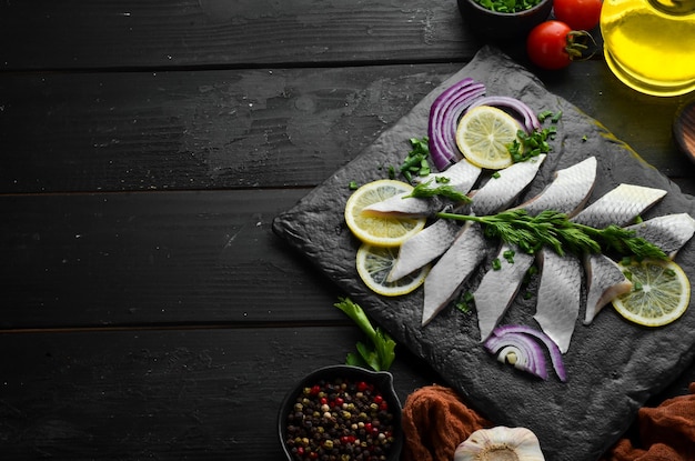 Salted herring with onion and lemon on a black stone board Top view Free space for your text