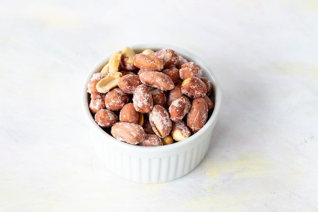 Salted peanuts in bowl on white wooden background