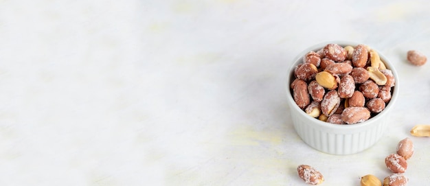 Salted peanuts in bowl on white wooden background