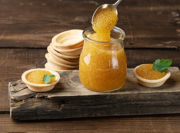 Salted pike caviar in a glass jar on a wooden board, top view