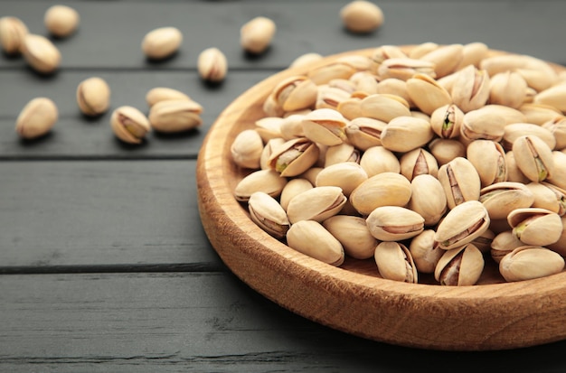 Photo salted pistachios for beer on black background healthy delicious pistachios in wooden plate