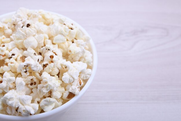 Salted popcorn in a bowl on a wooden table. Top view.