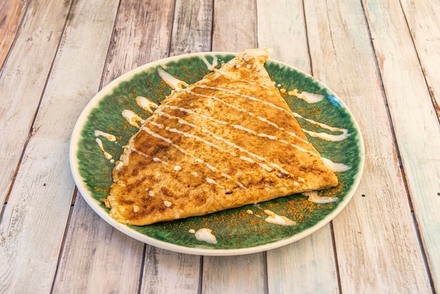 Salty French crepe sprinkled with red curry on green plate and wooden table