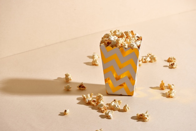 Salty fresh crusty homemade popcorn in golden paper cup in the fashion beige surface