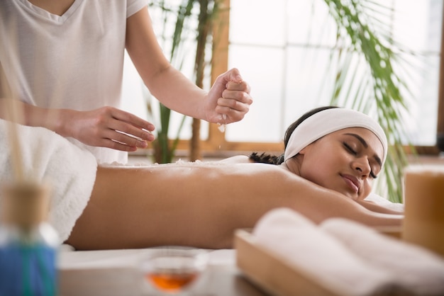 Salty massage. Professional female masseuse holding salt while putting it on her clients back