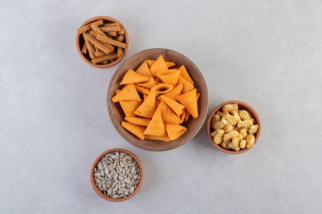 Salty snacks in bowls placed on a beige table .