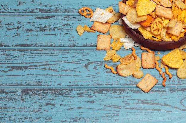 Photo salty snacks. pretzels, chips, crackers on wooden table. unhealthy products