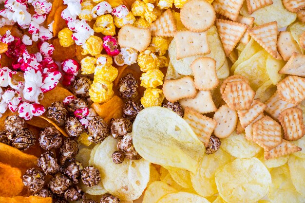 Salty and sweet popcorn and chips on the white background, low angle view