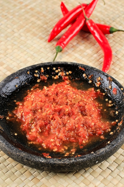Sambal Tomat of Sambel Terasi. Een populaire Indonesische kruiderij gemaakt van rode chilipepers en tomaat, geserveerd met traditionele mortel met rode chili op de achtergrond