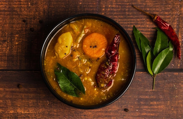 Foto sambar, un curry vegetariano misto disposto su una ciotola nera su uno sfondo di legno. sambar.