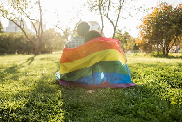 Same-sex couple in LGBT flag sitting in park