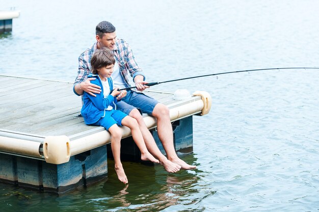 Samen afschieten. Bovenaanzicht van vader en zoon die samen op de kade vissen