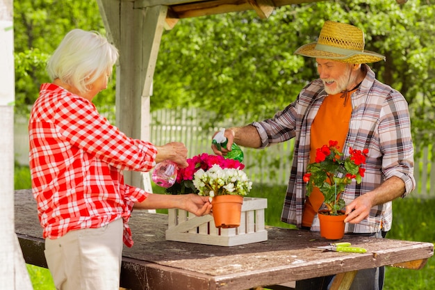 Samen bloemen water geven. Paar stralende, vrolijke gepensioneerden die zich vrolijk voelen terwijl ze samen bloemen water geven