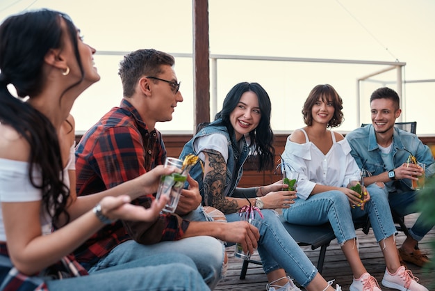 Samen chillen jonge vrolijke mensen kletsend en cocktails drinkend zittend op de