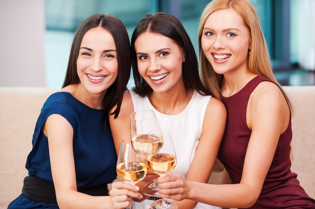 Samen genieten van een geweldige tijd. Drie mooie jonge vrouwen in avondjurk zittend op de bank