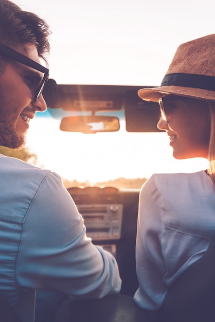 Samen genieten van elke minuut. Achteraanzicht van een gelukkig jong stel dat naar elkaar kijkt terwijl ze in hun cabrio zitten