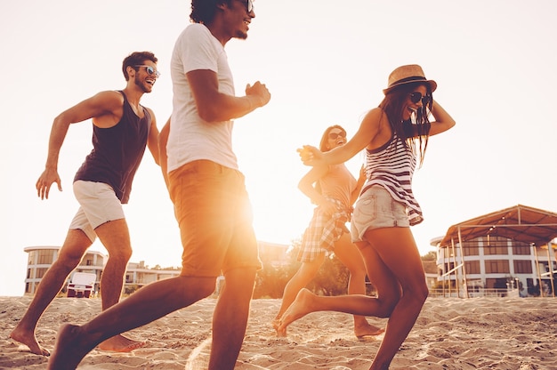 Samen genieten van leuke tijd. groep jonge vrolijke mensen die langs het strand rennen en er gelukkig uitzien