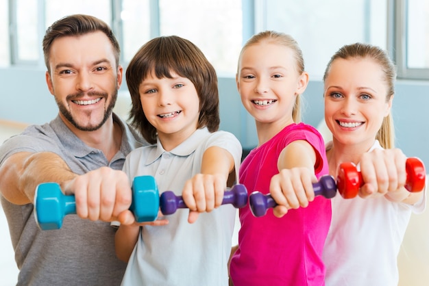 Samen gezond leven. gelukkige familie die verschillende sportuitrusting vasthoudt terwijl ze dicht bij elkaar staan in de gezondheidsclub