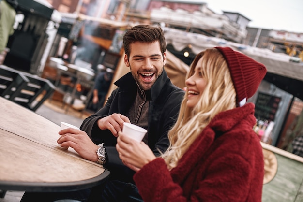 Samen koffie drinken. jong stel spreekt terwijl ze buiten warme dranken, thee of koffie drinken. ze zitten op de bank