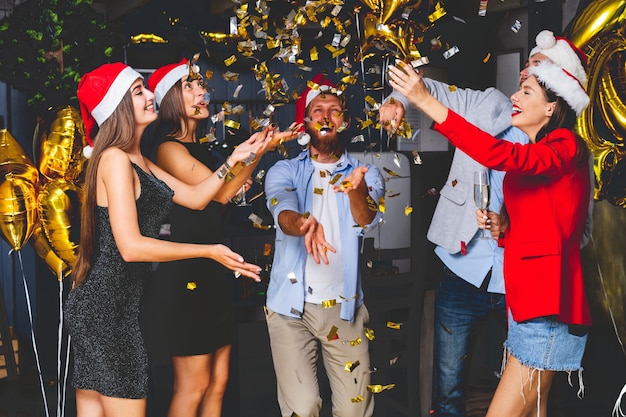 Foto samen nieuwjaar vieren. groep mooie jonge mensen in santa hoeden kleurrijke confetti gooien en op zoek gelukkig