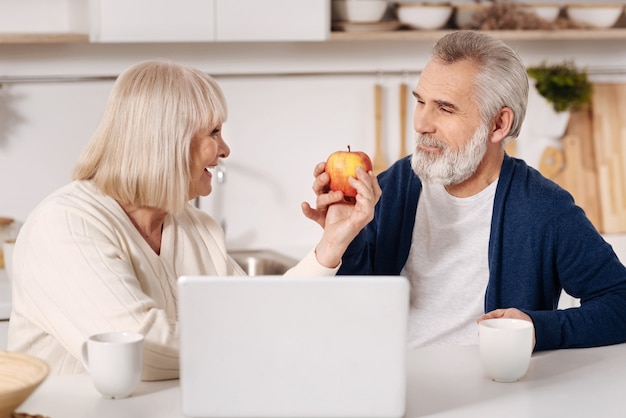 Samen plezier maken. Charmant blij oud paar om thuis voor laptop te zitten en appel te houden terwijl het uitdrukken van liefde en elkaar bekijken