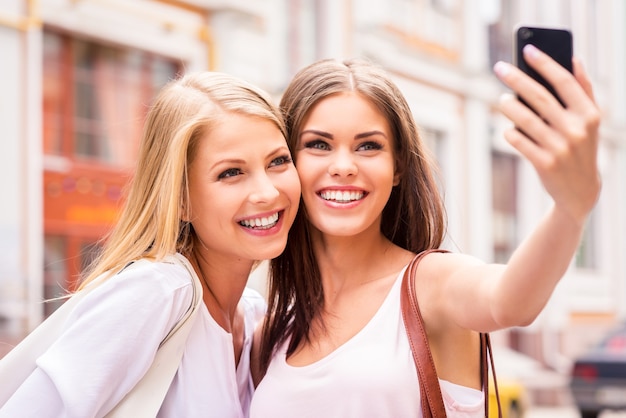 Samen plezier maken. twee mooie jonge vrouwen die selfie maken en glimlachen terwijl ze buiten staan