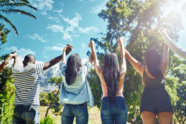 Samen staan we op Achteraanzicht van een groep jonge vrienden die triomfantelijk hun handen opsteken