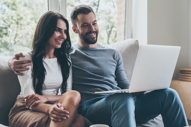 Samen surfen op het web. Mooie jonge verliefde paar kijken naar laptop en glimlachen terwijl ze samen op de bank zitten