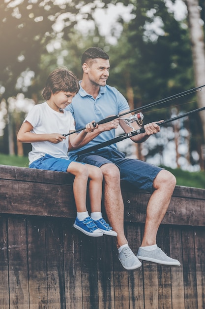 Samen vissen. Vrolijke vader en zoon vissen zittend op de kade