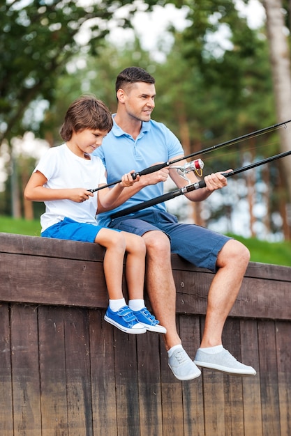 Samen vissen. Vrolijke vader en zoon vissen zittend op de kade