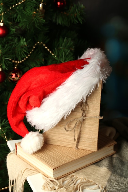 Samenstelling met boeken en geruite rode hoed op stoel op kerstboomachtergrond