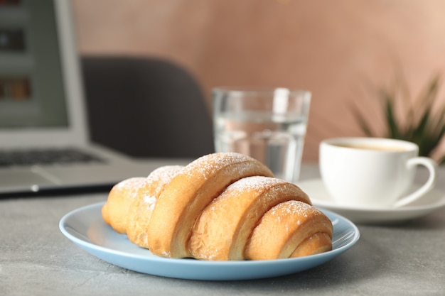 Samenstelling met croissant en computer op grijze tafel, close-up