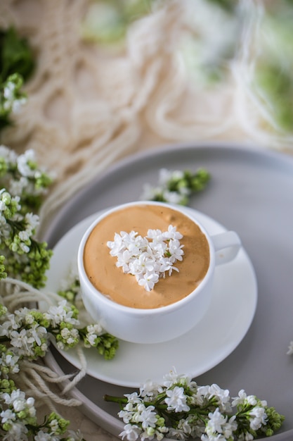 Samenstelling met de takken van lila en verse koffie met schuim in witte kop./