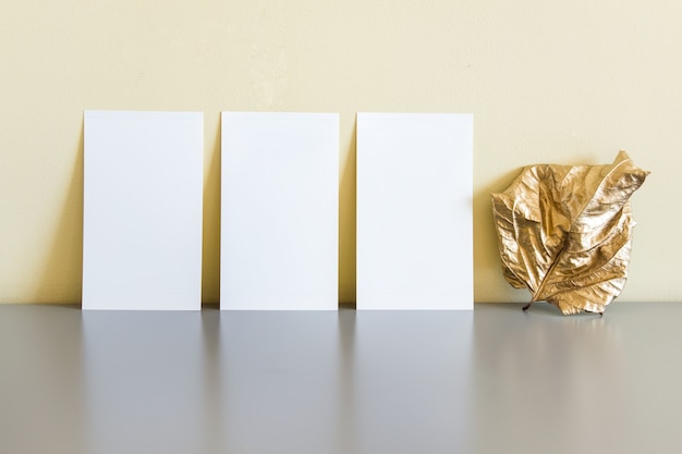 Samenstelling met drie kaarten en gouden droog blad staande op grijs reflecterend oppervlak.