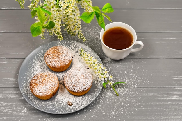 Samenstelling met een kopje thee cupcakes en witte kersen bloemen op een houten achtergrond