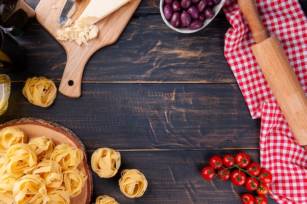 Samenstelling met ingrediënten voor de bereiding van Italiaanse pasta. Tomaten, Parmezaanse kaas, olijven, basilicum en rauwe pasta. Ruimte voor tekst