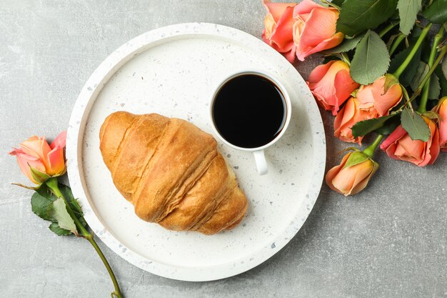 Samenstelling met marmeren dienblad, kopje koffie, croissant en rozen, bovenaanzicht