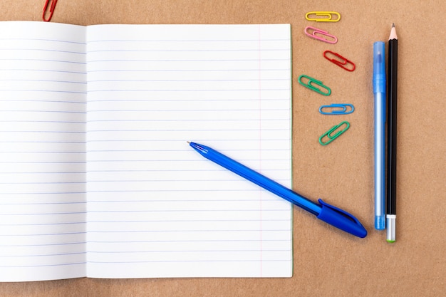Samenstelling met notebook blanco pagina kleurrijke potlood, marker en pen met kopie ruimte. Terug naar school concept op een ambachtelijke kartonnen achtergrond
