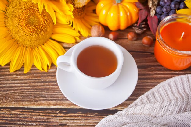 Samenstelling met pompoen, herfstbladeren, zonnebloem, kopje thee, plaid en bessen op de houten tafel