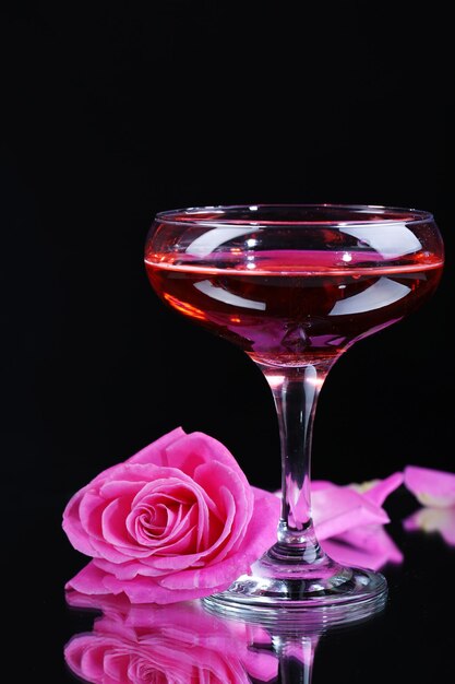 Samenstelling met roze mousserende wijn in glas en roos geïsoleerd op zwart