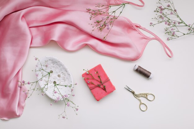 Samenstelling met roze zijden stof cadeau in ambachtelijke papier en draden en schaar op wit plat lag bovenaanzicht