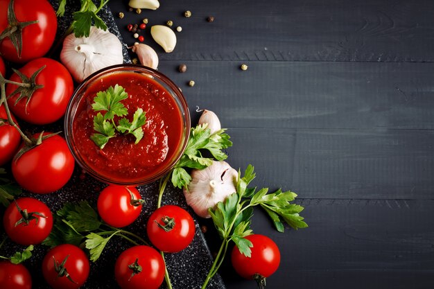 Samenstelling met tomaten, knoflook, peterselie, tomatensaus en peper op zwarte houten planken