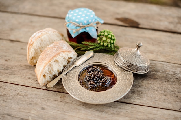 Samenstelling van de kegels jam in de zilveren plaat met een dop en gras pot, boomtak en brood in de buurt op de houten tafel