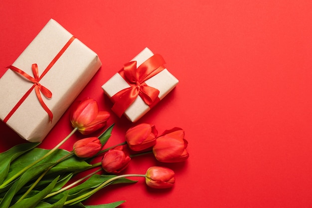Samenstelling van de lente. Boeket van rode tulpen en geschenkdoos op rode achtergrond.