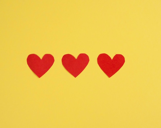 Samenstelling van drie rode harten op een gele achtergrond Plat gelegd