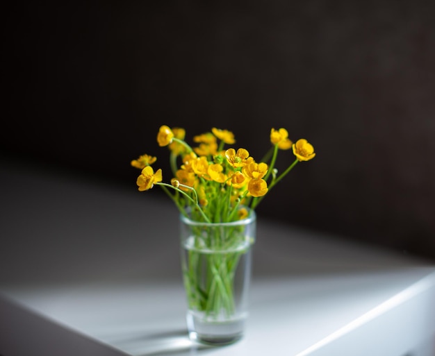 Samenstelling van felgele wilde bloemen in een glazen beker