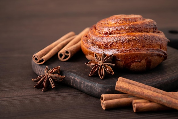 Samenstelling van gebakken kaneelbroodje op donkere houten tafel. Kaneelstokjes en anijsster op houten achtergrond